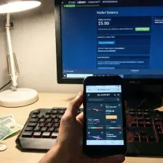 Na biurku leżą polskie banknoty i monety, obok klawiatury i lampki stoi monitor ze Steamem i telefon z aplikacją Skinport.